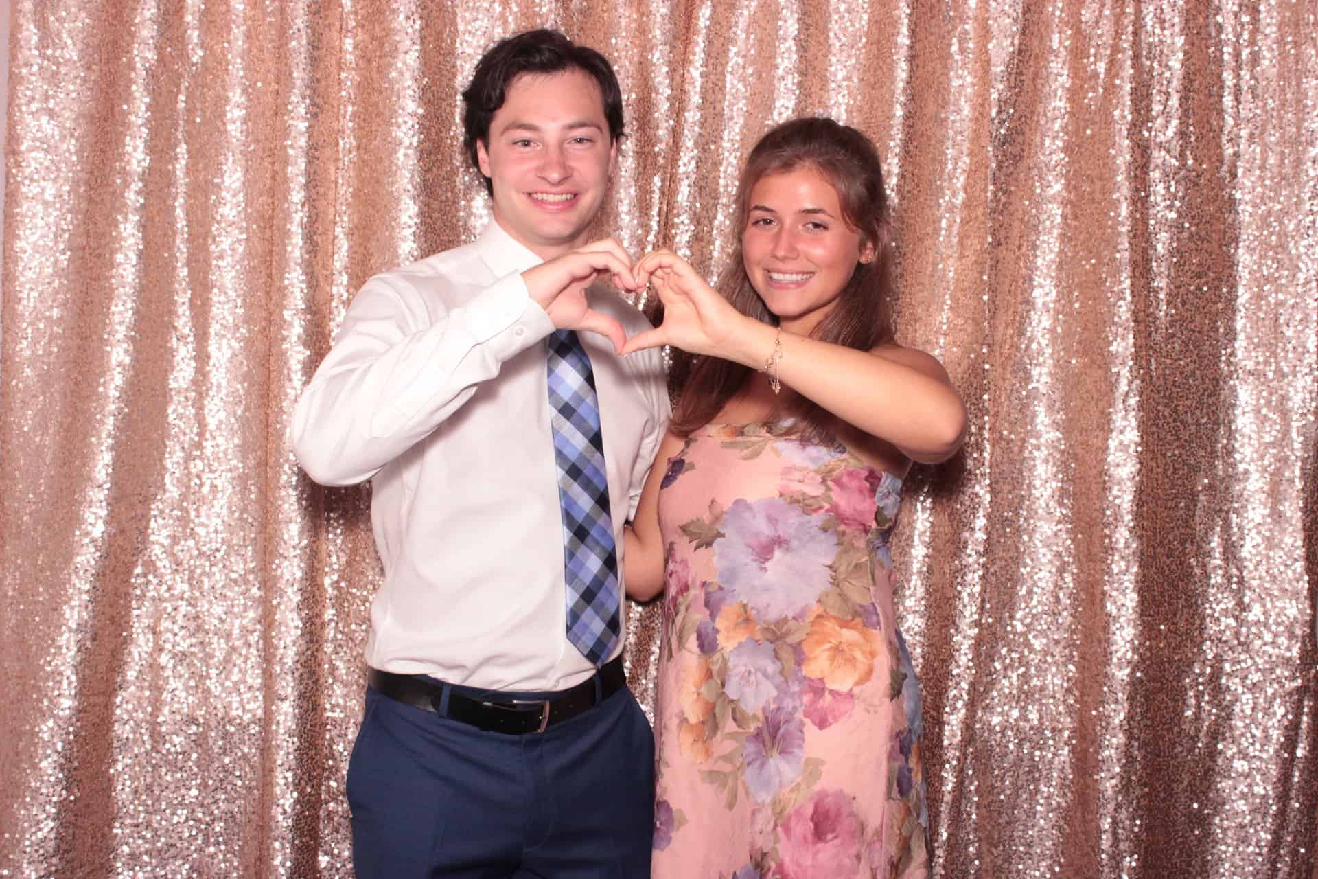 A couple making a heart shape with their hands inside a photo booth