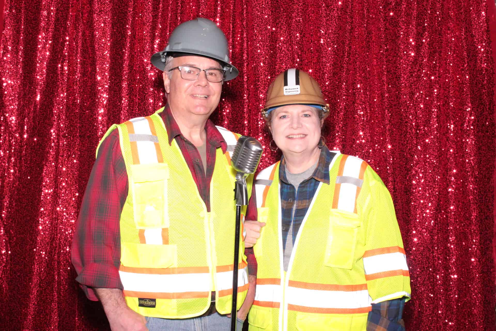 two adults in safety vests taking a photobooth photo in front of a microphone